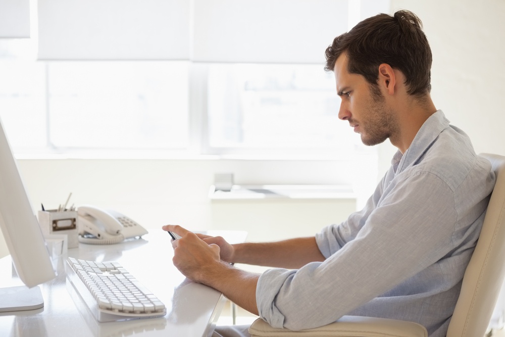 Casual businessman sending a text at his desk in his office