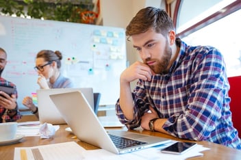 Concentrated bearded young man using laptop while his friends studying together